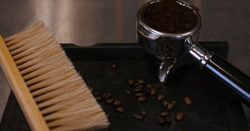 Natural bristle counter brush beside a dosed portafilter and coffee beans on a grinder tray
