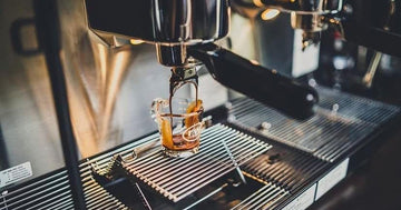 Espresso extracting into a glass on a commercial machine, sized for peak cafe demand