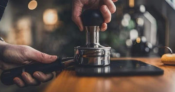 Barista tamping a dosed portafilter on a counter mat in a Dubai style cafe