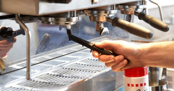 Barista cleaning an espresso machine group head with a Rattleware group brush